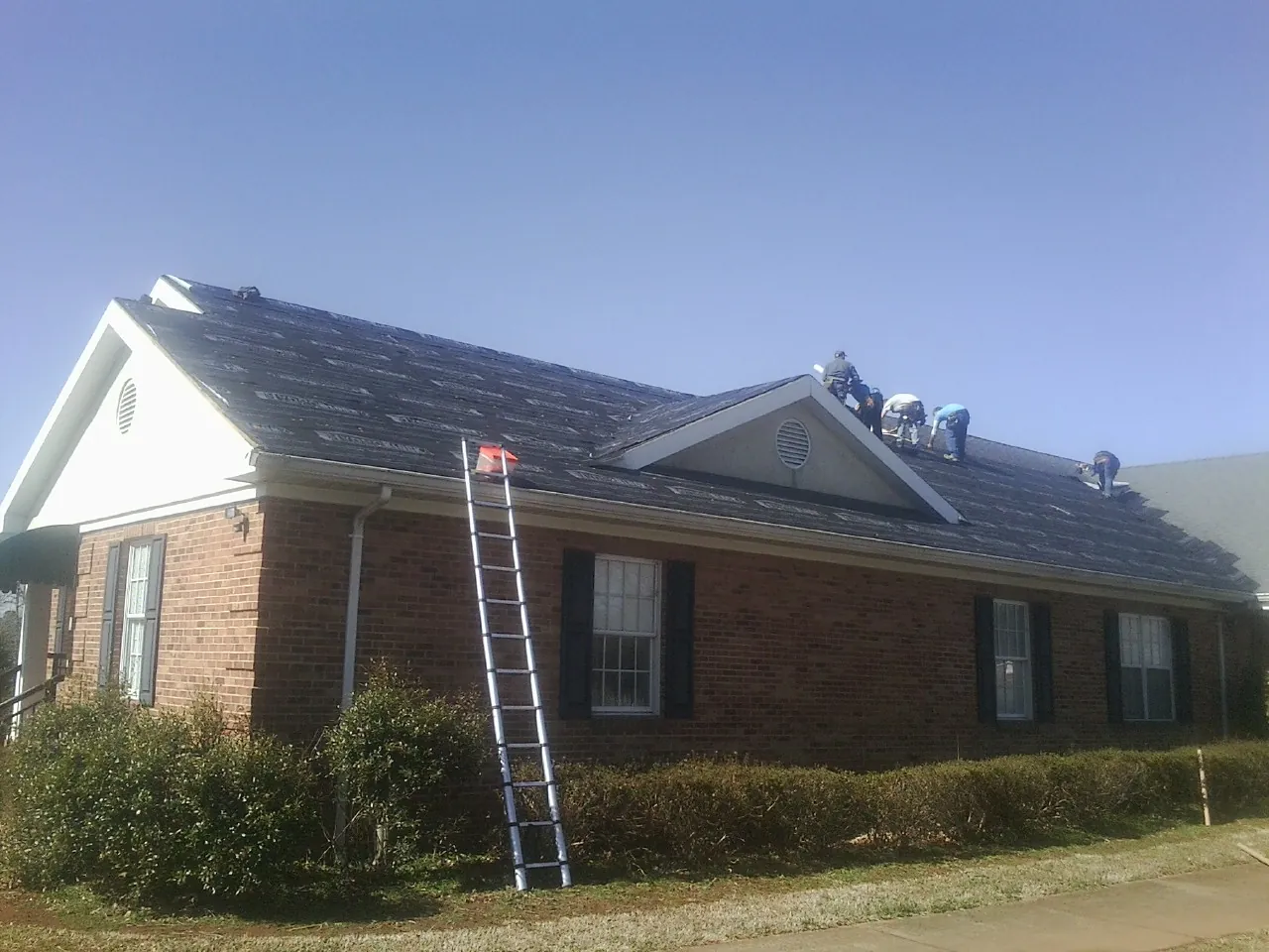 Crew tearing shingles off a brick ranch roof with a ladder set — Emergency Roof Repair work by our crew in Pinopolis