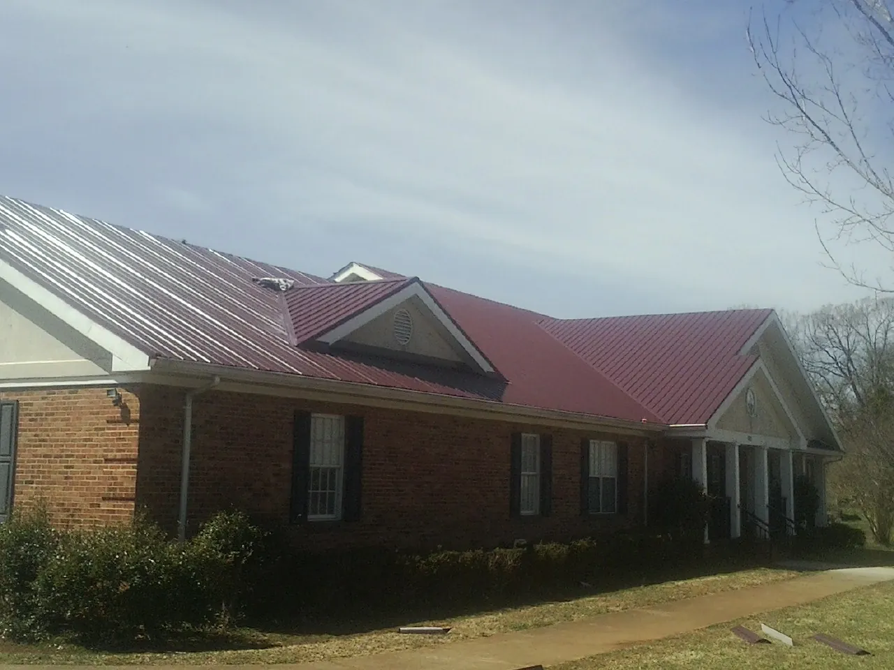 Red metal roof with gabled entries on a long brick building, from a Hail Damage Roof Repair job in Pinopolis