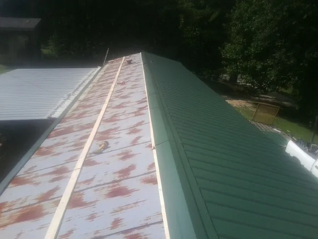 Old rusted panels beside newly installed green metal roofing — Wind Damage Roof Repair by Roofing Brothers in Pinopolis