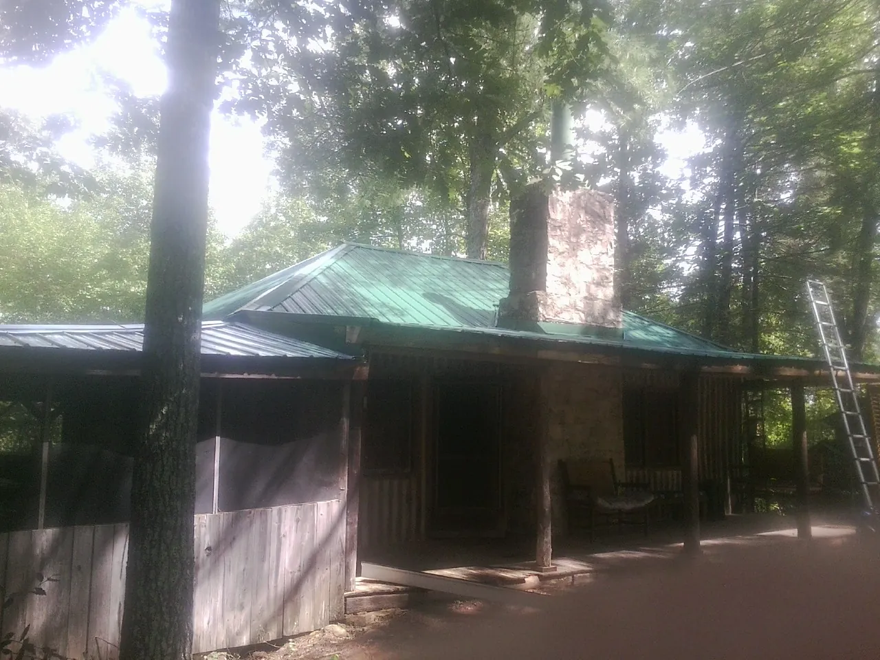 Green metal roof and stone chimney above a log cabin porch in Pinopolis