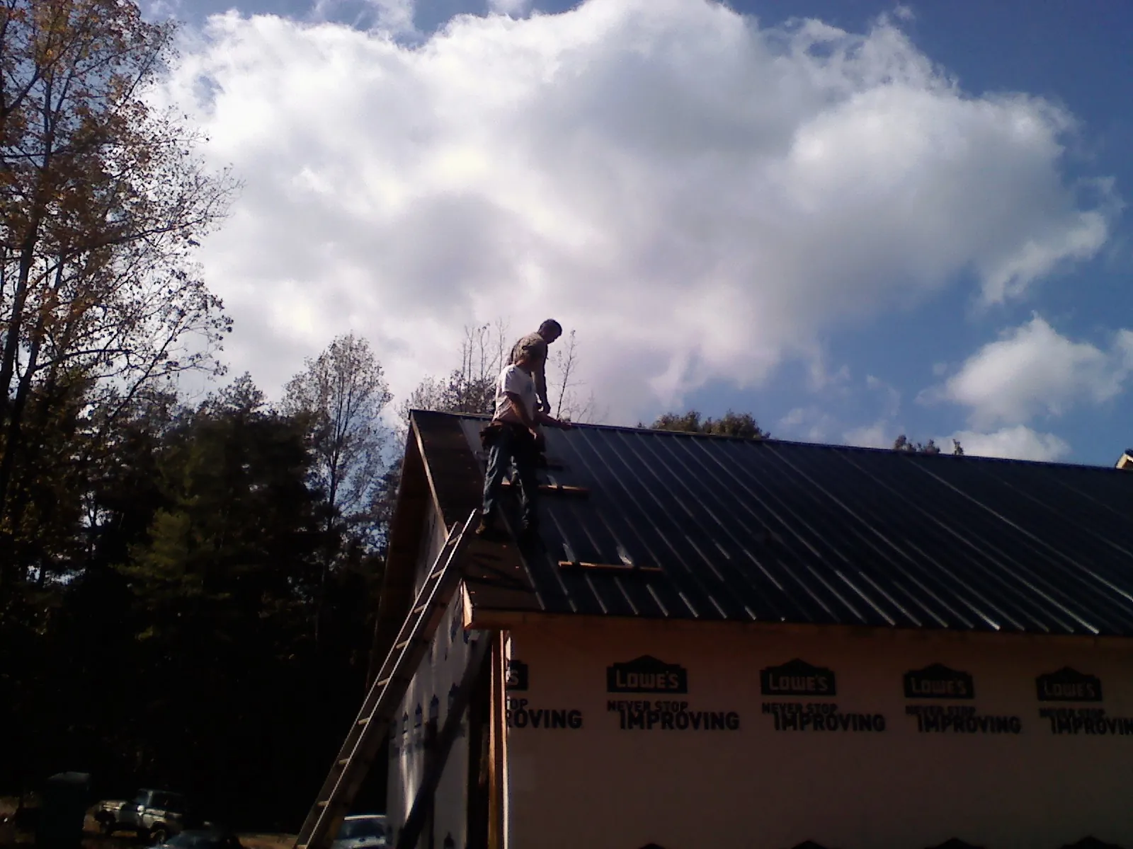 Roofer fastening dark metal panels high against a cloudy sky, from a Roof Inspection job in Pinopolis