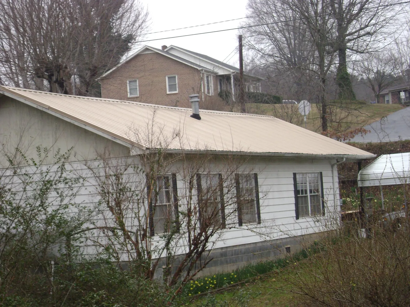 Tan metal roof on a white sided house set into a hillside — Commercial Roofing by Roofing Brothers in Pinopolis