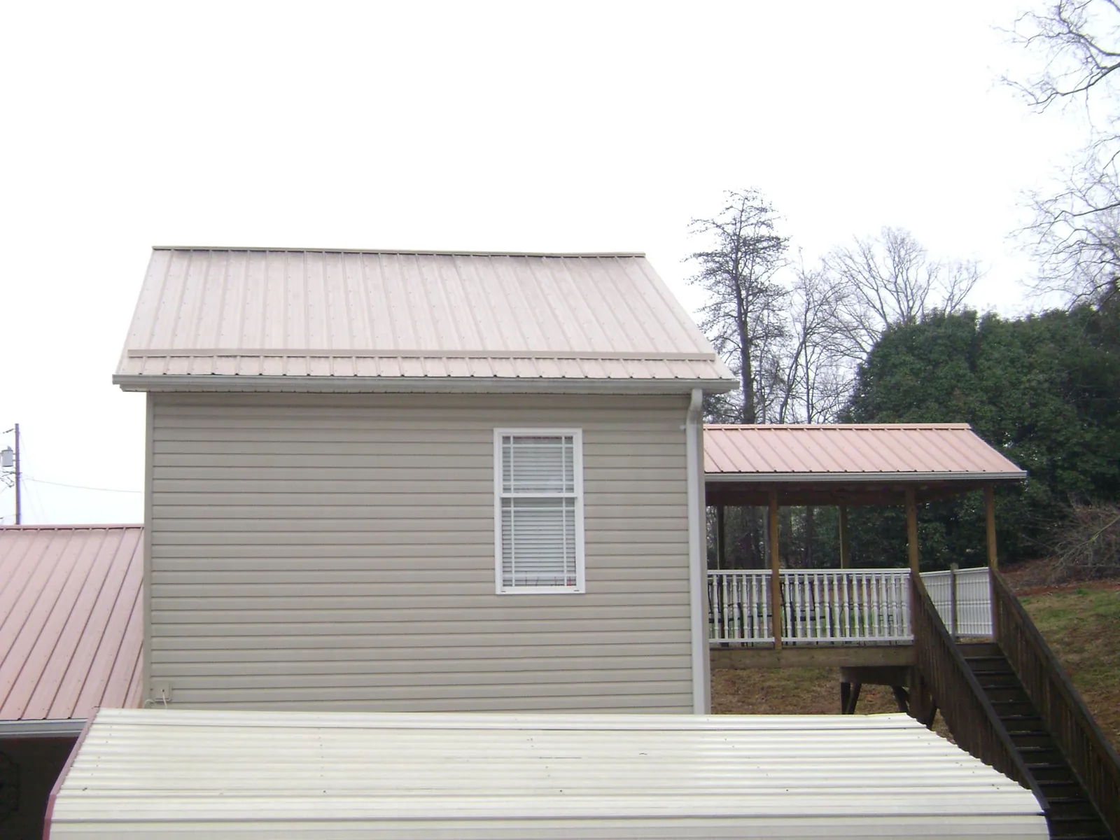 Tan metal roofs on a two story addition and attached porch, from a Roof Replacement job in Pinopolis